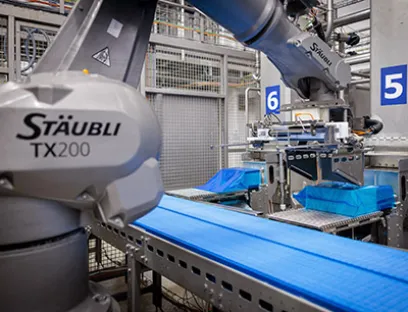 Der Arbeitsablauf in der Zelle beginnt mit dem Ausschieben des Käseblocks aus dem Turm in den aufgespreizten Folienschlauch, Bild: Stäubli / Marco Prosch Die hygienegerechten Stäubli Roboter verpacken pro Stunde bis zu 5,5 Tonnen Käse