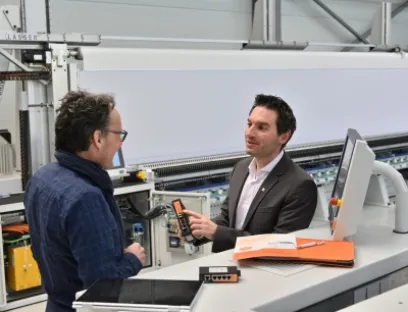 Vor der Stickmaschine MVD71 erklärt Peter Hirt (rechts im Bild), Segment Manager Machinery & Automation Sales, Patrik Schwarz, Softwareentwickler und Projektverantwortlicher bei Lässer, die Vorteile des Industrial Security Routers von Weidmüller, Bild: Weidmüller Vor der Stickmaschine MVD71 erklärt Peter Hirt, Segment Manager Machinery & Automation Sales, Patrik Schwarz, Softwareentwickler und Projektverantwortlicher bei Lässer, die Vorteile des Industrial Security Routers von Weidmüller