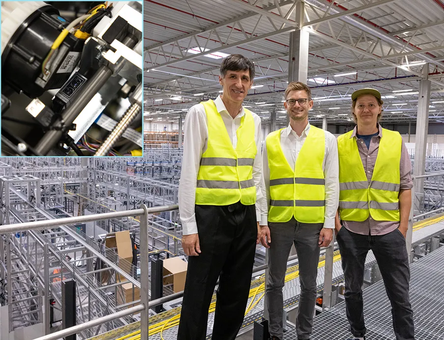 Intralogistik: Hier arbeiten mehr Roboter als Menschen. Mathias Magg, Teamleiter Robotics bei Advastore (re.) führt Peter Jürgen Tittes (mi.) und Christoph Kreidl (li.) von Baumer durch das vollautomatisierte Auslieferungscenter; Oben links: Beim Blick in den offenen Transportshuttle erkennt man den kompakten „OT300“, der mit seiner Reichweite bis 1,8 Meter an dieser Stelle die senkrechte Kollisionsvermeidung sicherstellt